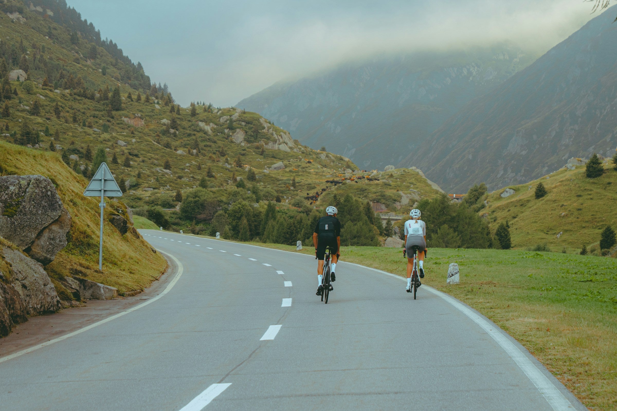 Two cyclists on a mountain road in Switzerland. Editorial photograph by Jack White on Unsplash, not a product or customer photograph.